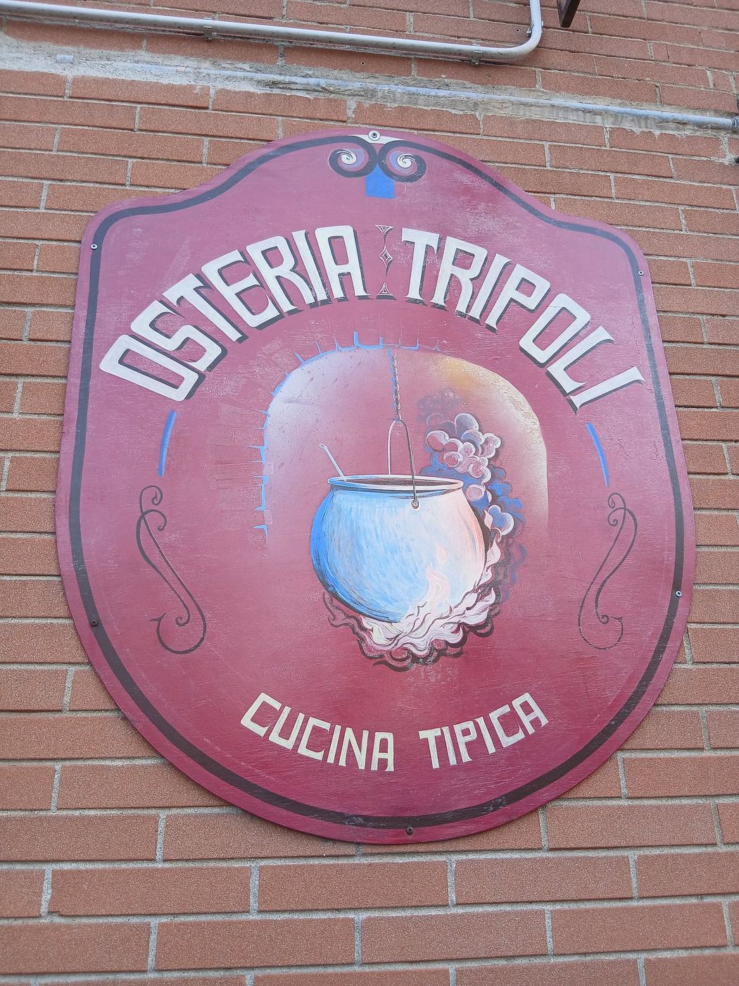 Hand-painted Osteria Tripoli sign on a brick wall: a red shield with a cooking pot and the words Cucina tipica