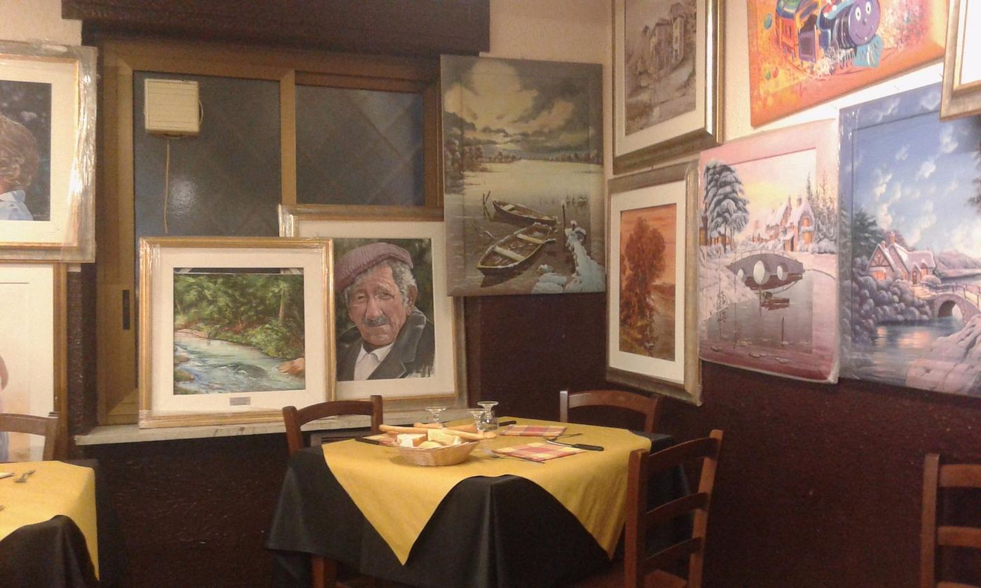A corner of the dining room with paintings on the walls and a table laid with a yellow tablecloth