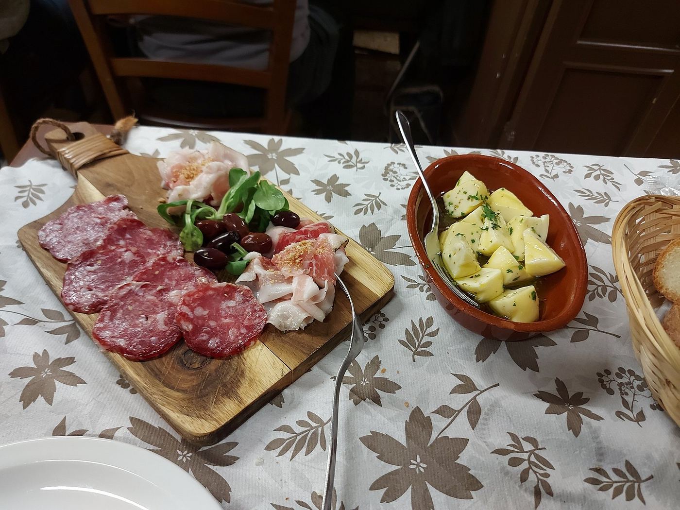 Board of cured meats with a bowl of pickled vegetables on a floral tablecloth